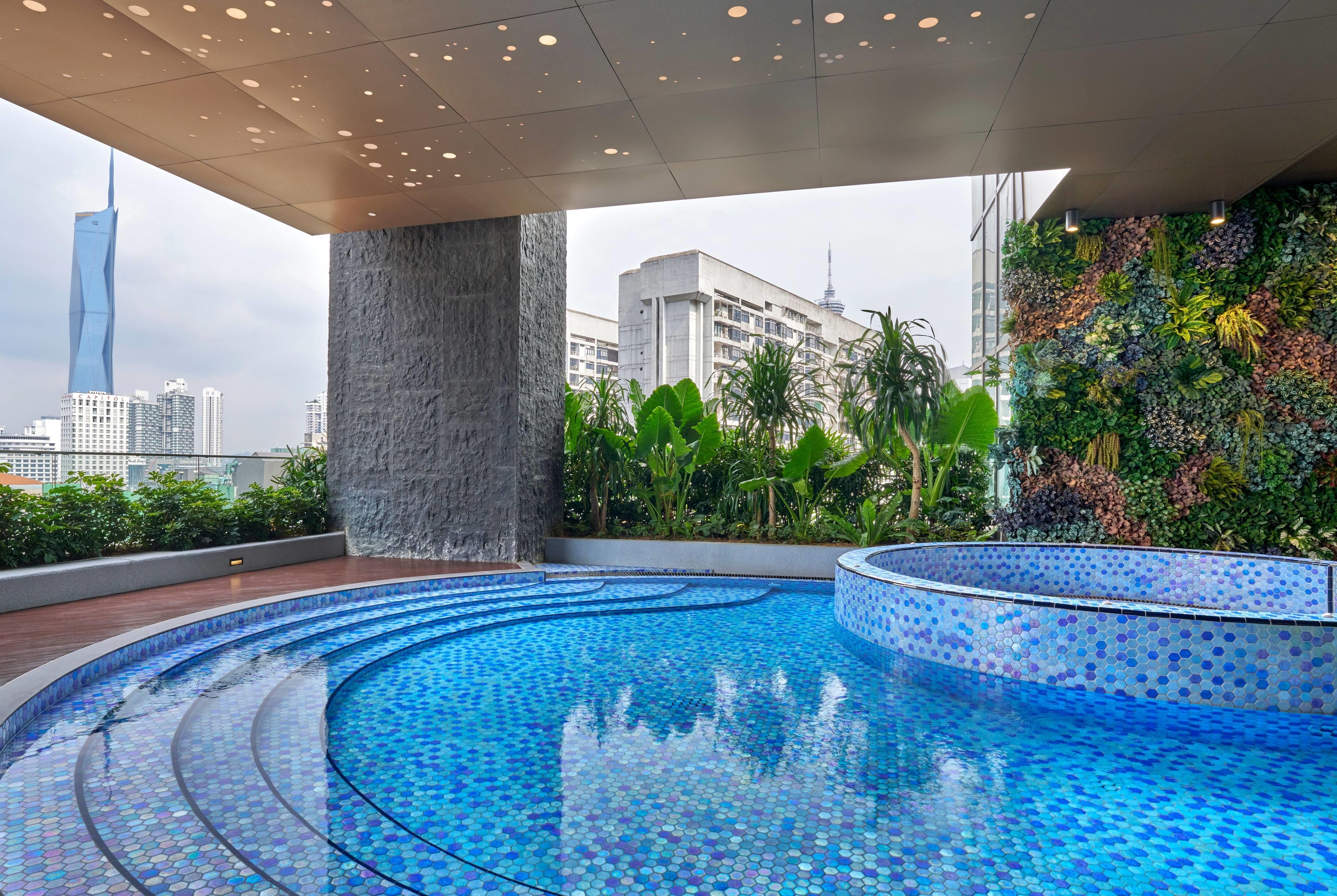 A rooftop pool with a cityscape view, surrounded by greenery and a modern building.