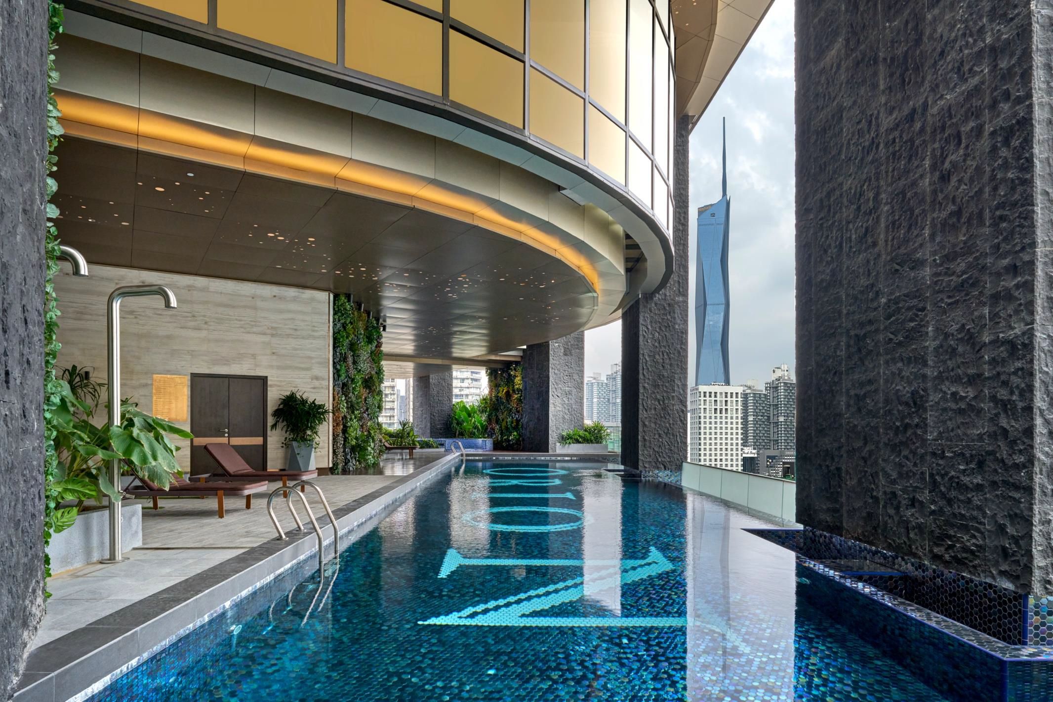 Piscina interior moderna com design de água azul cristalina, rodeada por paredes de pedra e plantas internas.