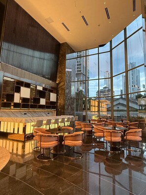 A modern interior with a bar area, seating, and large windows offering a view of the cityscape.