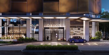 A modern hotel entrance with a car parked in front, a well-lit facade, and a sign reading 'ORION RESIDENCE'.