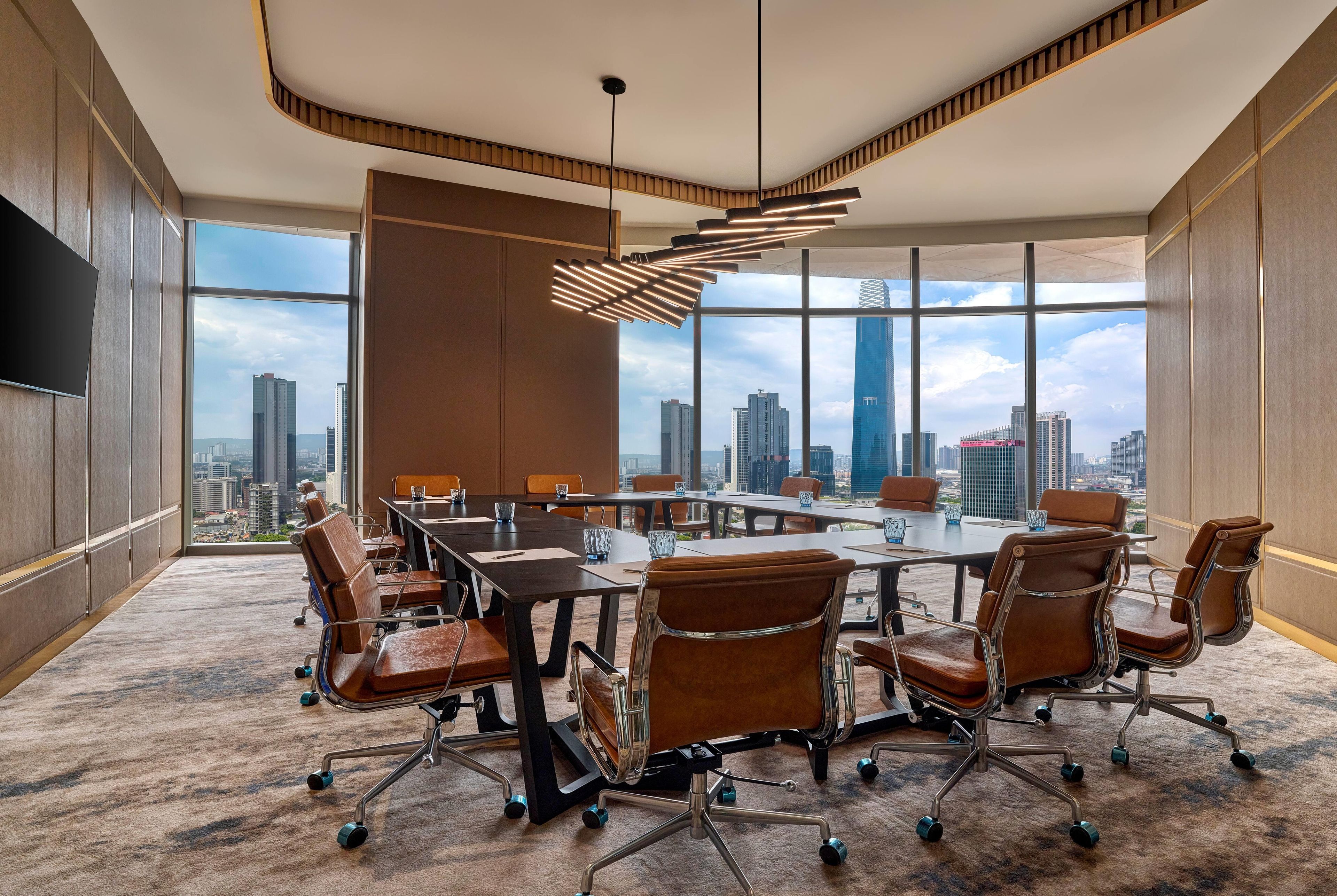A conference room with a panoramic city view, modern furniture, and a unique ceiling light fixture.
