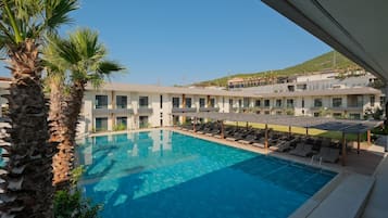A hotel with a swimming pool, sun loungers, and a view of a hilly landscape.