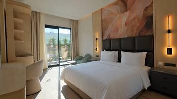 Habitación de hotel moderna con una cama grande, una zona de estar con sillas, vistas al exterior a través de un ventanal y un muro decorativo.