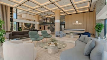 A modern hotel lobby with a central seating area, a reception desk, and a staircase leading to an upper level.