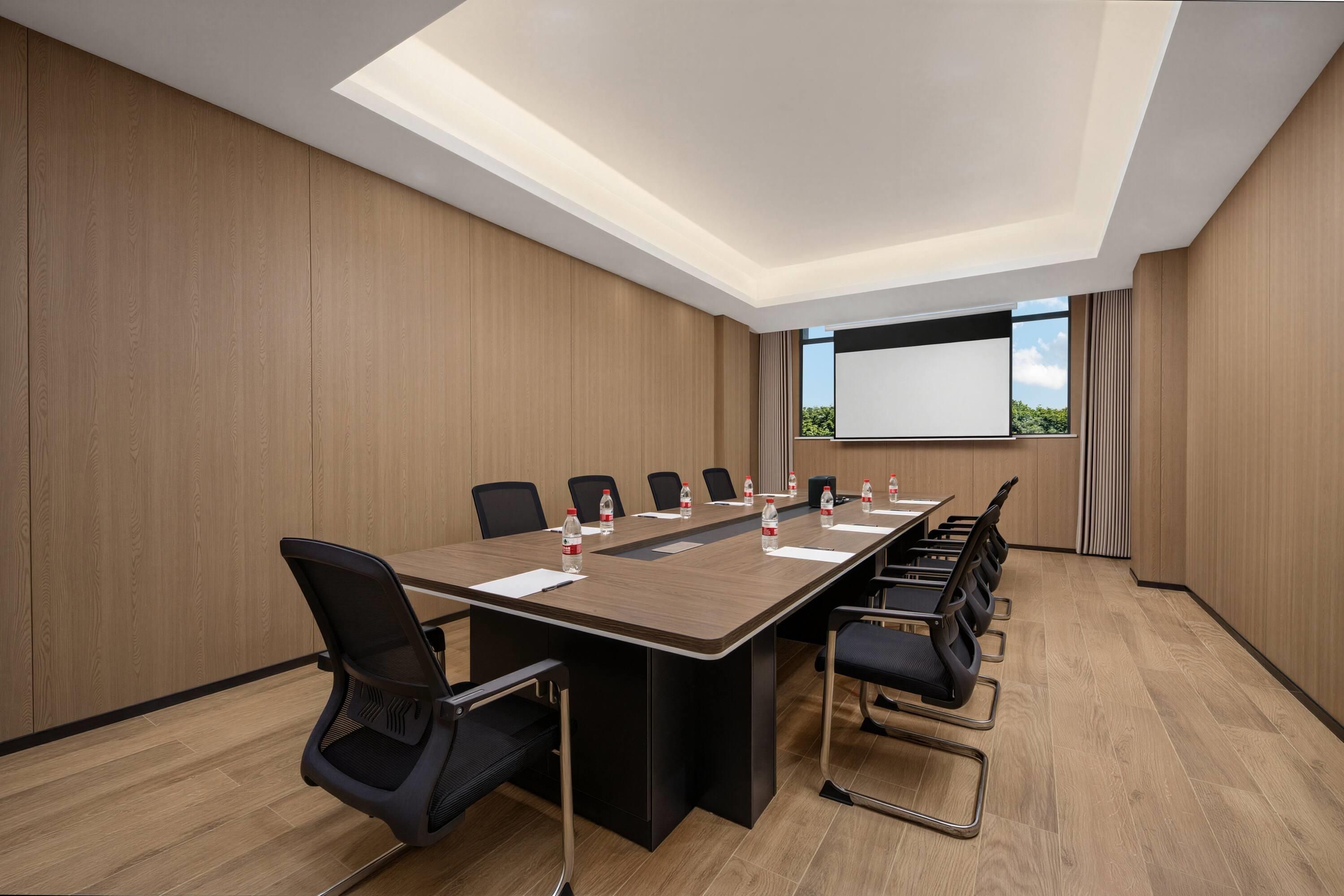 Una sala de conferències amb una taula llarga, cadires, una pantalla de projector i vista cap a l'exterior.