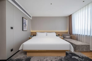 Habitació d'hotel moderna amb un llit gran, taules de nit, un sofà i un finestra ampla amb cortines.