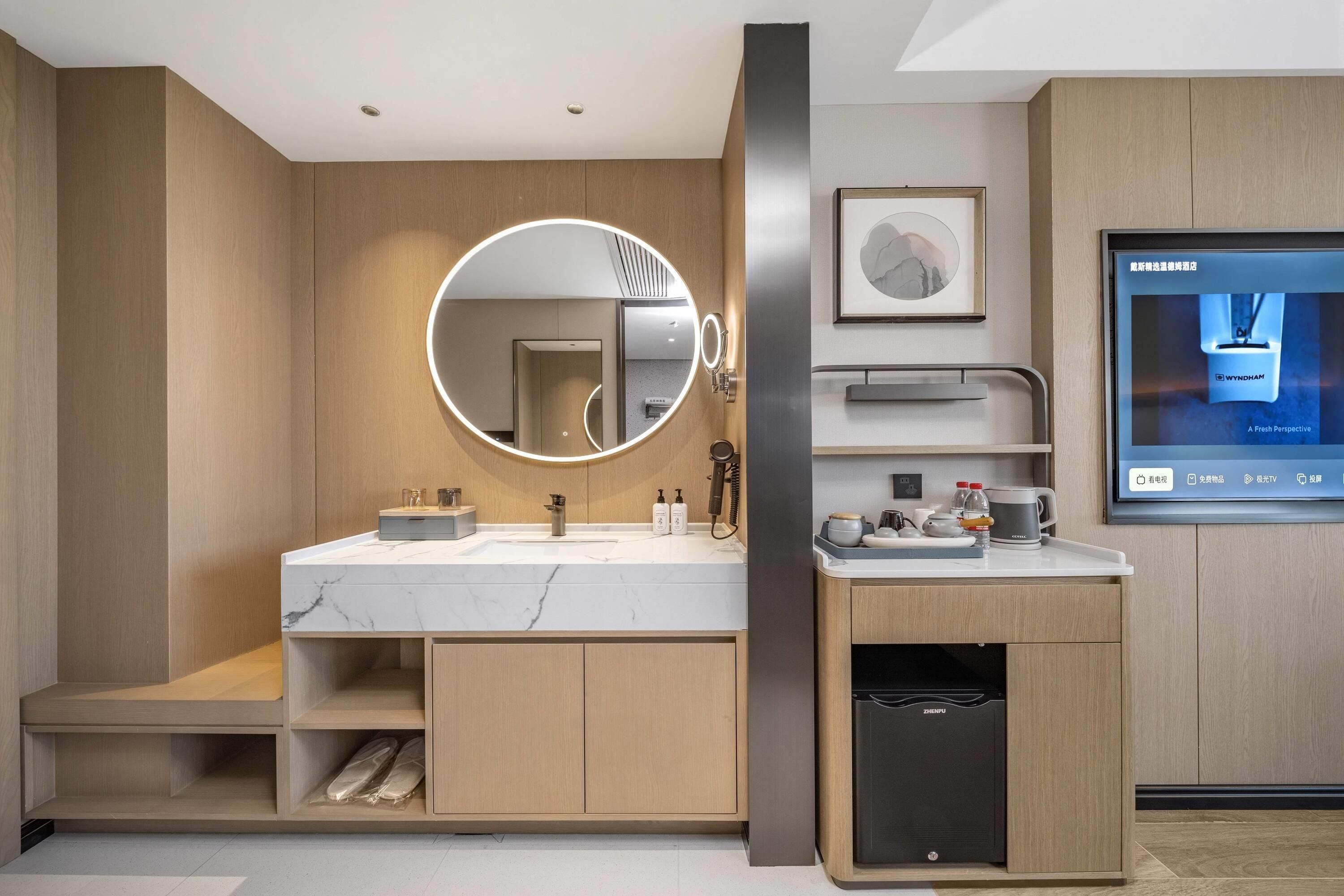 Un baño moderno con tocador de mármol, un espejo redondo con iluminación, un lavabo y un calefactor empotrado.