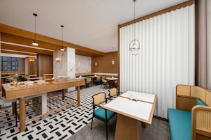 A modern restaurant with a long communal table, individual tables, and a patterned floor.