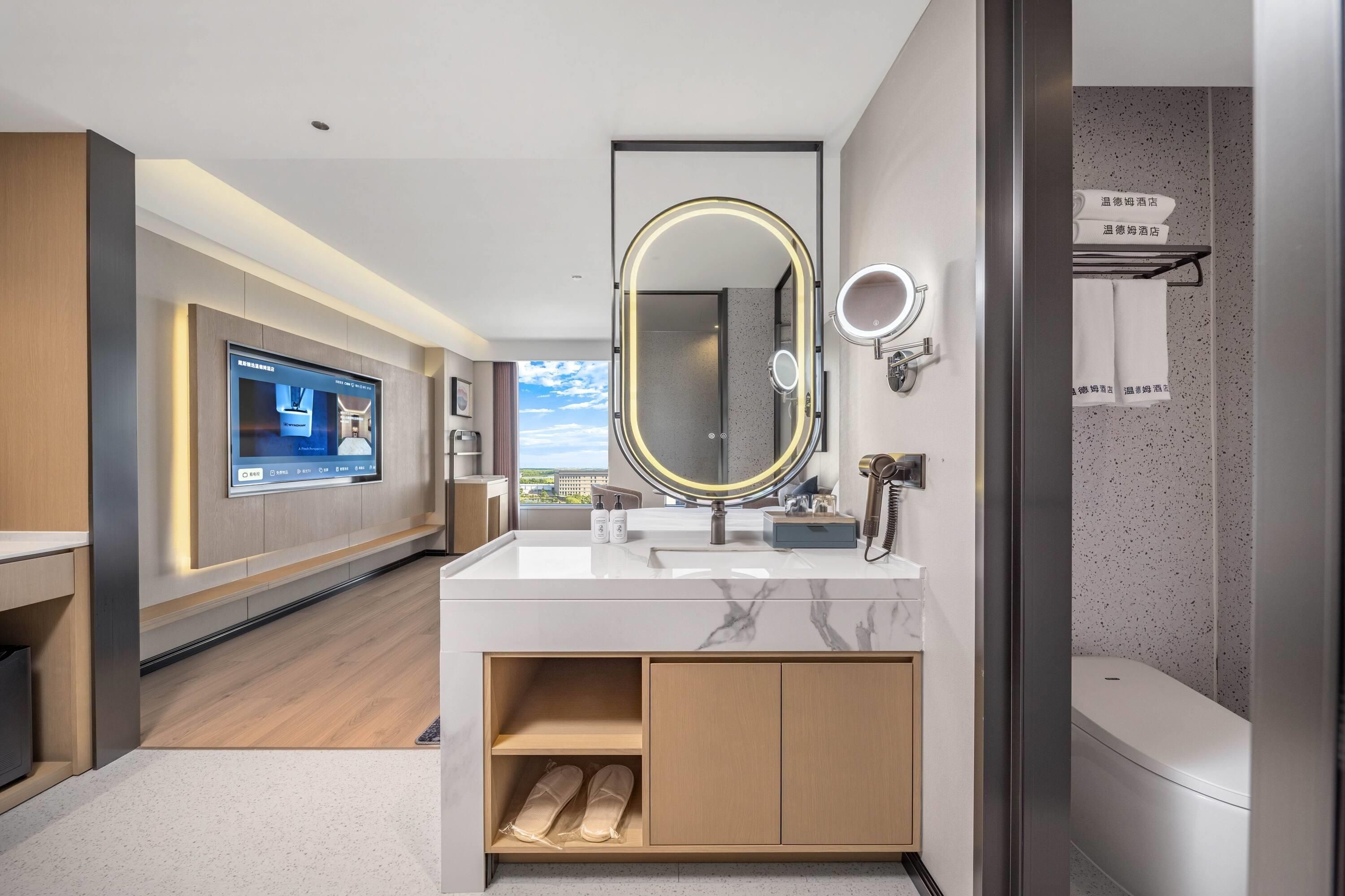 Une salle de bain d’hôtel moderne, dotée d’un grand miroir, d’un meuble-lavabo et d’un téléviseur qui affiche une vue sur la pièce.