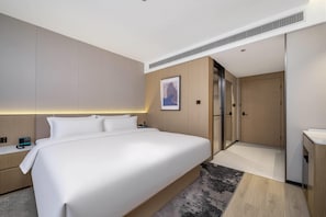 A modern hotel room with a large bed, bedside tables, a wardrobe, and a bathroom with a shower and toilet.