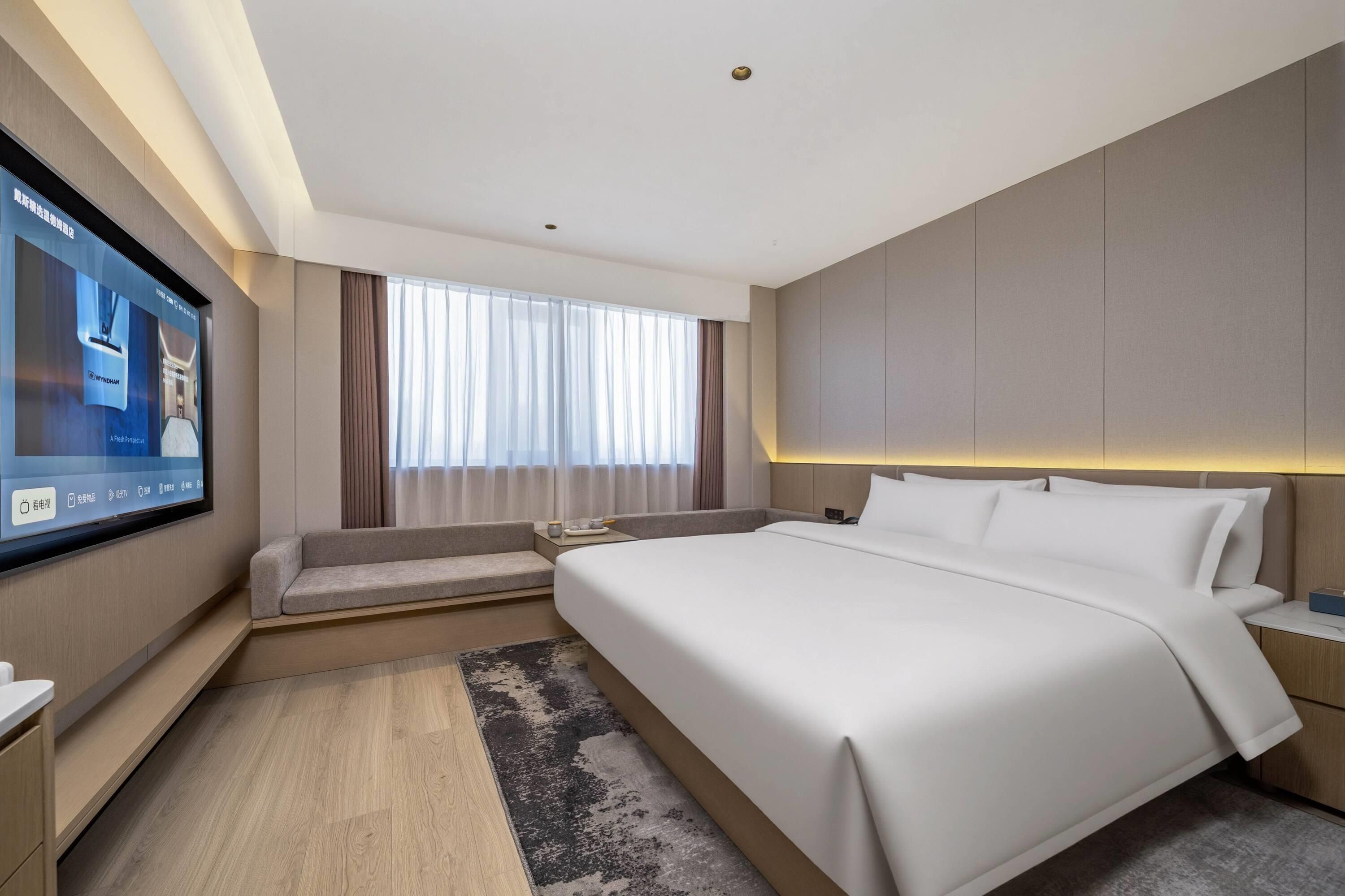 Una habitación de hotel moderna con una cama grande, un televisor de pantalla plana montado en la pared y un área de estar con un sofá y una mesita.
