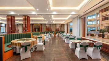 A spacious banquet hall with tiered seating, round tables, and a high ceiling with recessed lighting.