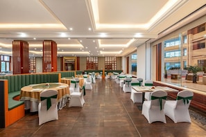 A spacious banquet hall with tiered seating, round tables, and a high ceiling with recessed lighting.