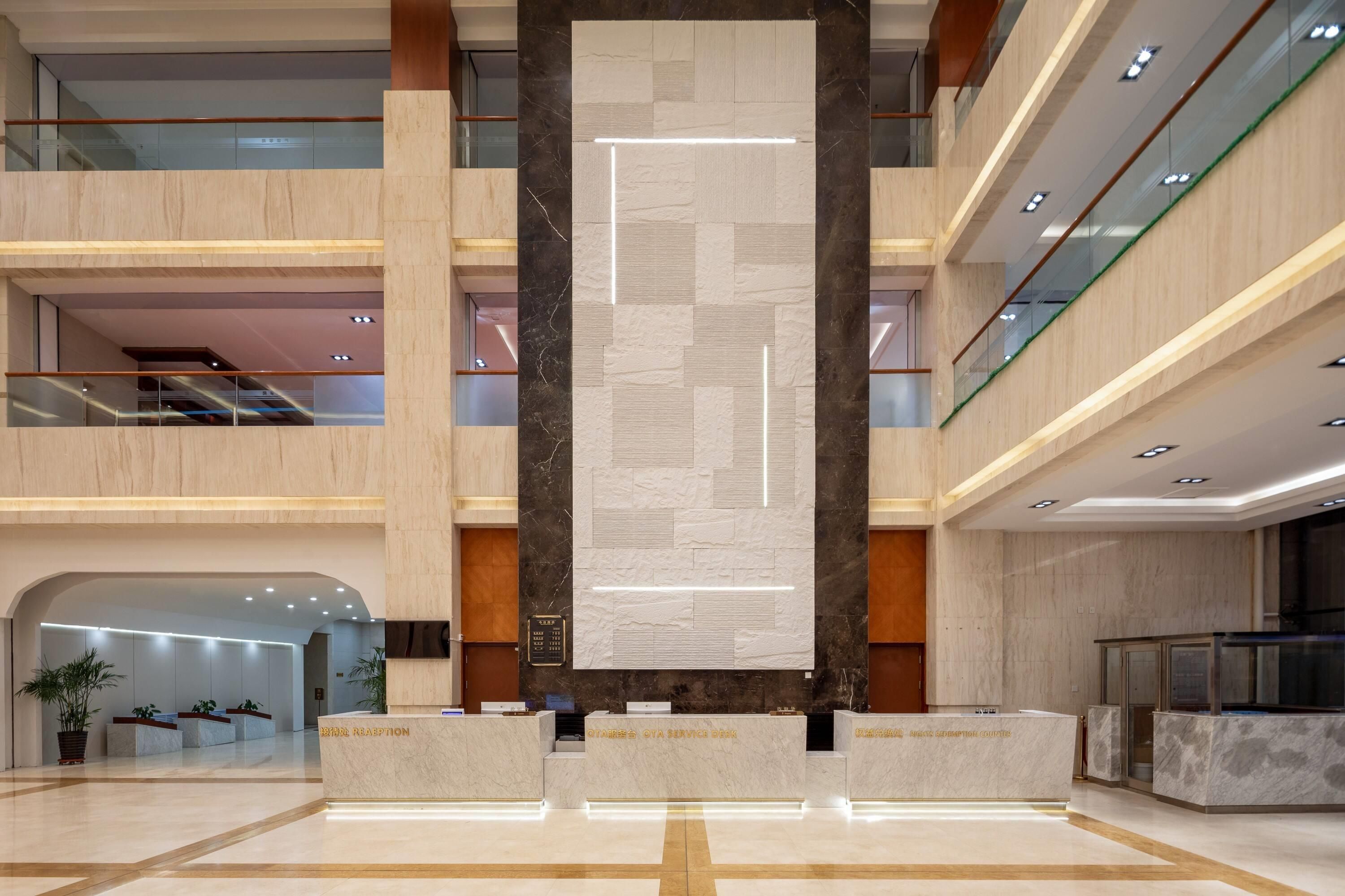 A multi-level hotel lobby with a reception desk, a large vertical display, and a staircase.