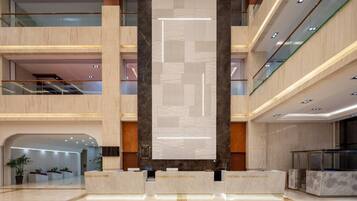 A multi-level hotel lobby with a reception desk, a large vertical display, and a staircase.