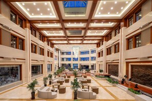 A spacious lobby with multiple seating areas, a central chandelier, and a high ceiling with recessed lighting.