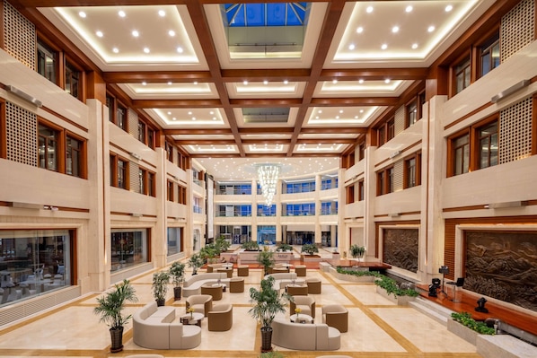 A spacious lobby with multiple seating areas, a central chandelier, and a high ceiling with recessed lighting.