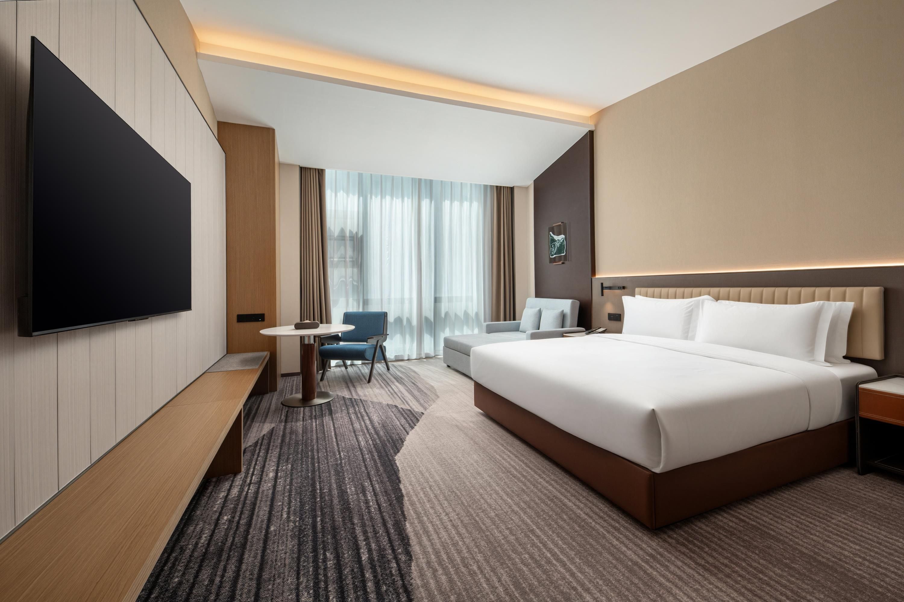 Een hotelkamer met een groot bed, een flatscreen televisie, een bureau met stoel en een raam met gordijnen.