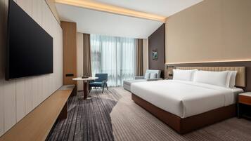 Een hotelkamer met een groot bed, een flatscreen televisie, een bureau met stoel en een raam met gordijnen.