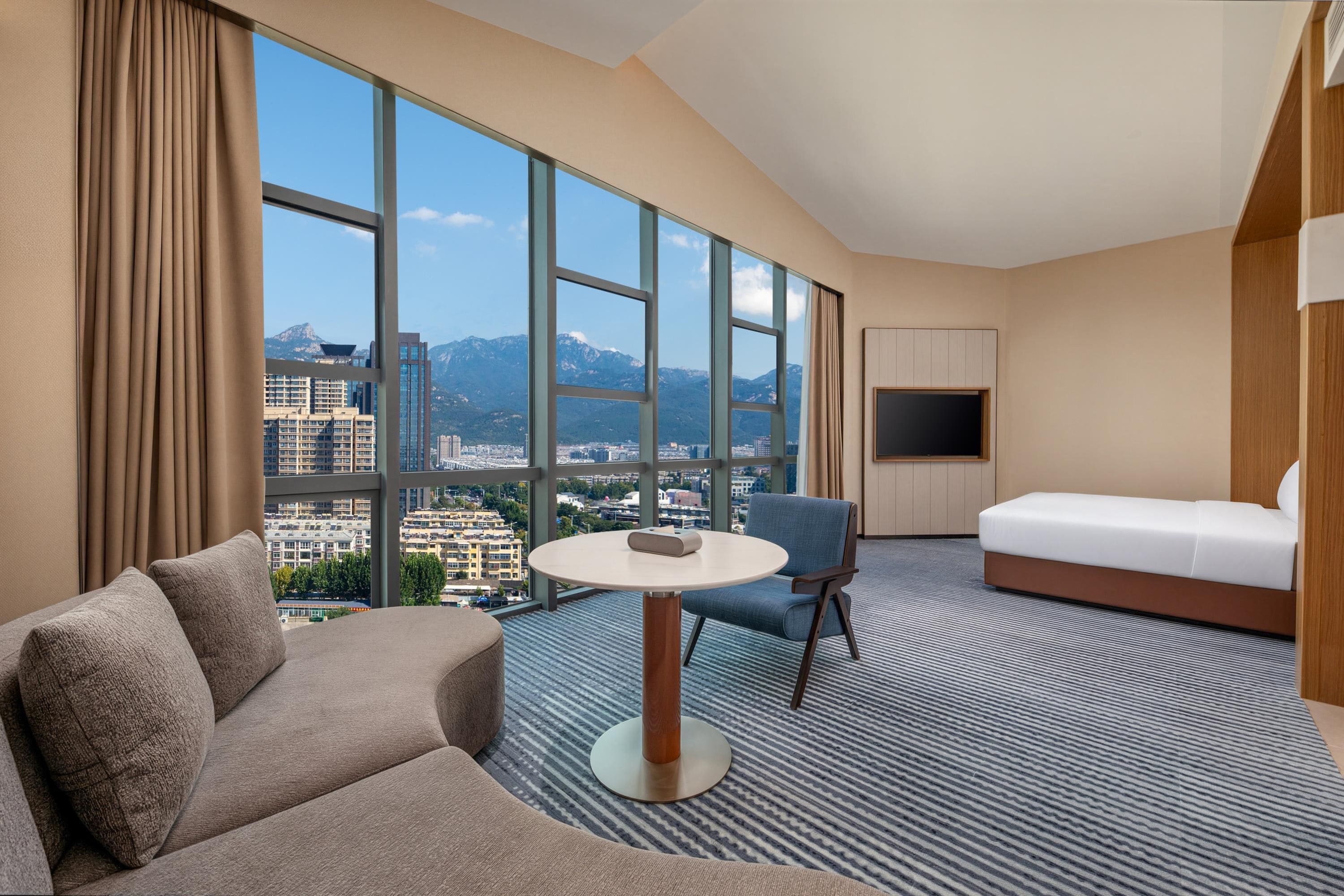A hotel room with a large window, a sofa, a round table, a chair, and a bed.