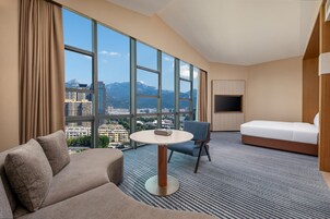 A hotel room with a large window, a sofa, a round table, a chair, and a bed.