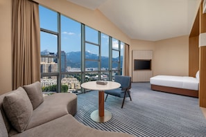 A hotel room with a large window, a sofa, a round table, a chair, and a bed.