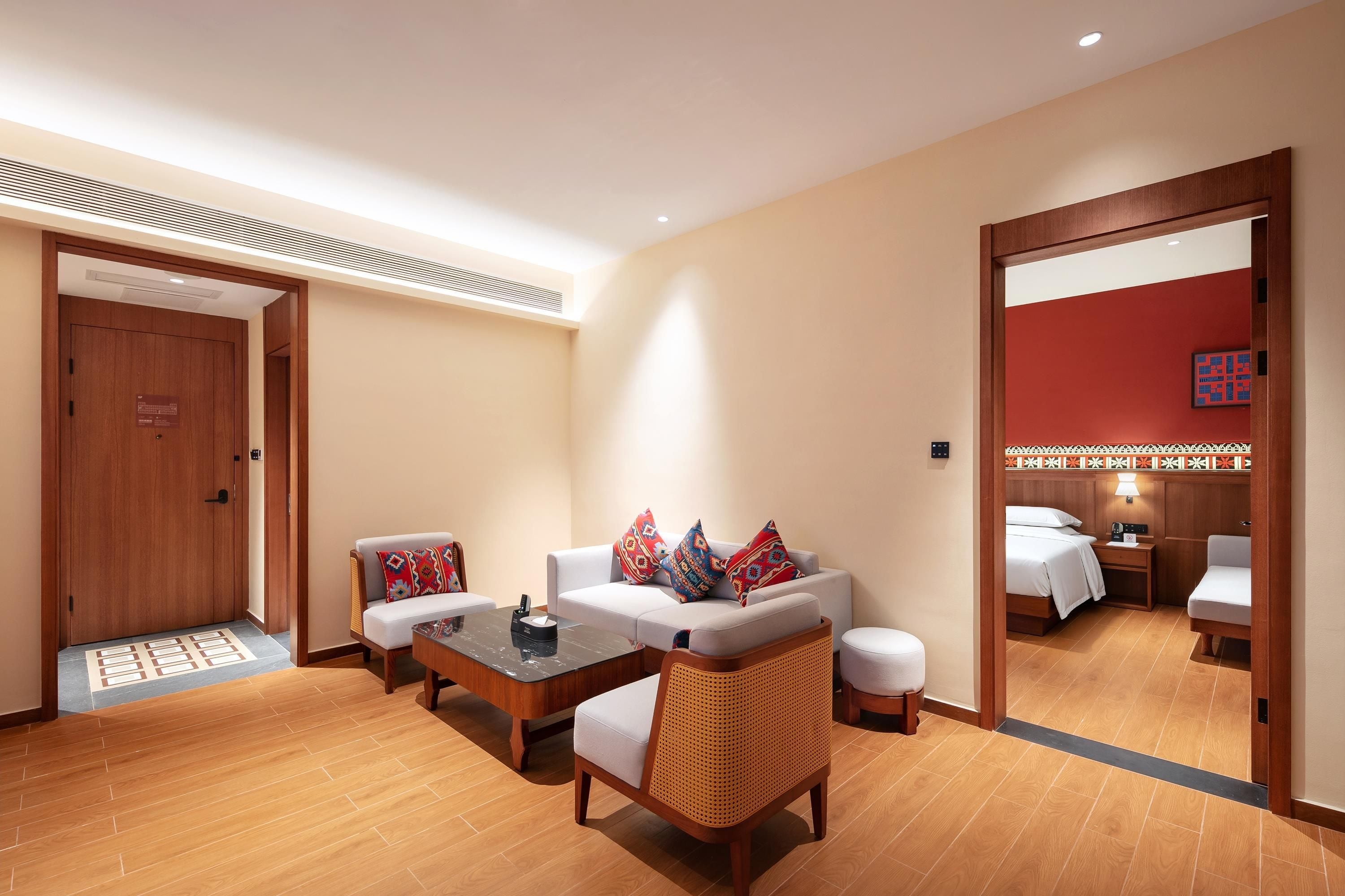 Habitación de hotel con sofá, mesa de centro, silla de mimbre, cama y baño visible a través de una puerta abierta.