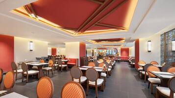 Un restaurante espacioso con varias zonas de comedor, techos altos con diseños geométricos y mobiliario moderno.
