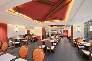Un restaurante espacioso con varias zonas de comedor, techos altos con diseños geométricos y mobiliario moderno.