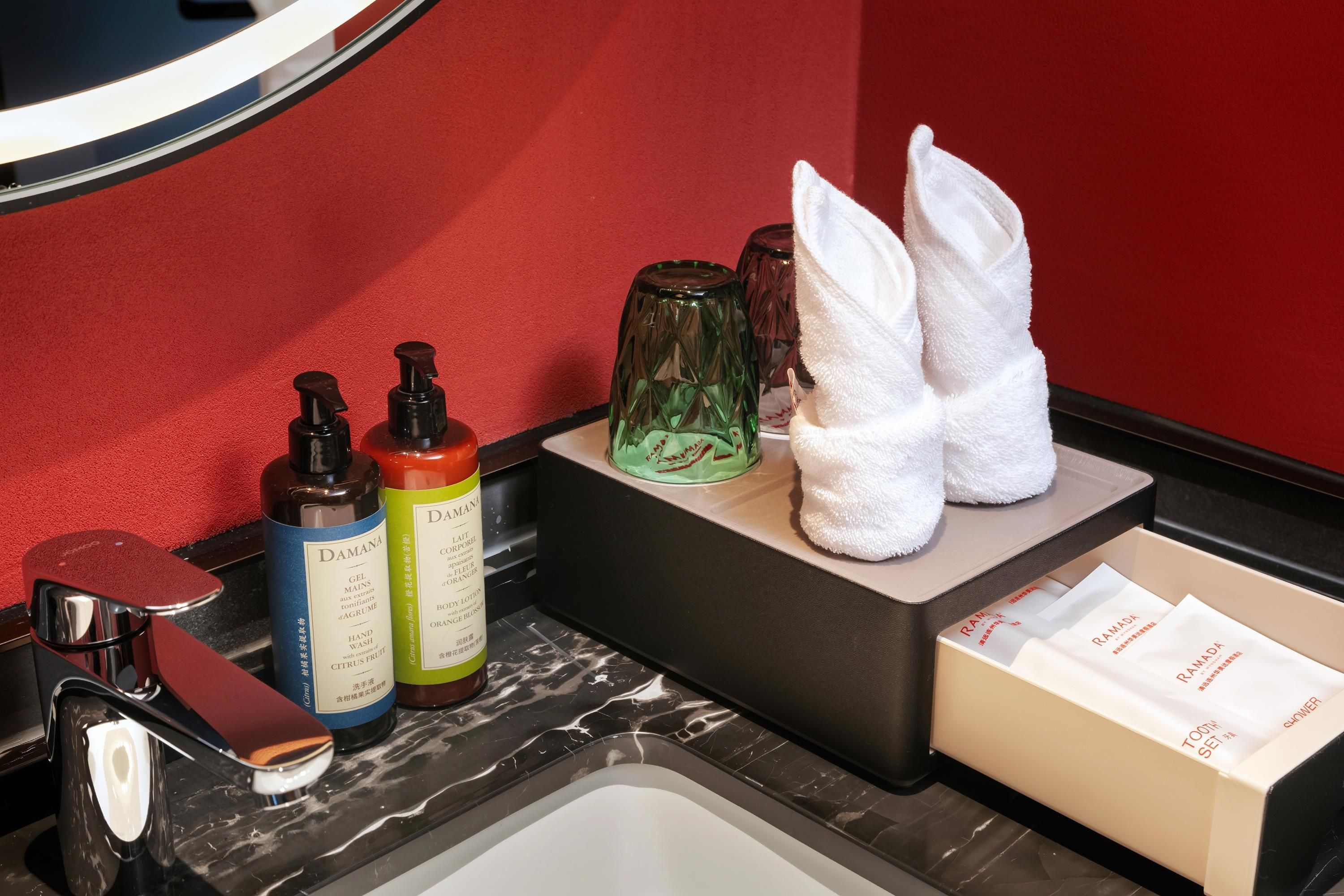 Un meuble-lavabo de salle de bain avec des articles de toilette, un distributeur de savon liquide, un flacon de crème pour les mains, une bouteille en verre verte et une serviette blanche.