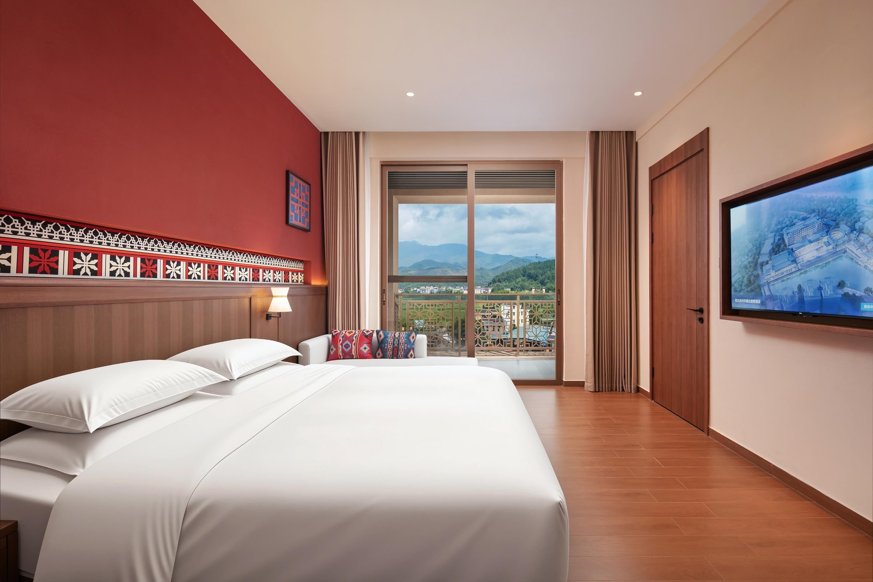 A hotel room with a large bed, a television mounted on the wall, and a balcony with a view of the city.