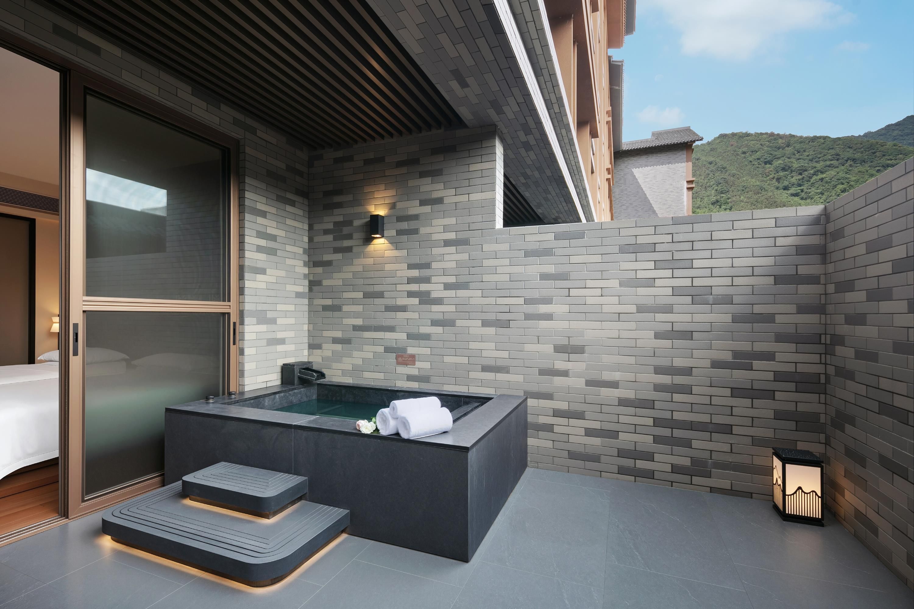 A modern outdoor spa area with a hot tub, seating, and a view of a mountainous landscape.