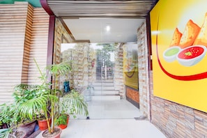 A corridor with tiled walls, potted plants, and a large poster on the right. - Hotel O DH Road Ernakulam (Kanayannur)
