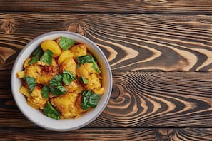 A bowl of food with potatoes and greens on a wooden table. - Hotel O DH Road Ernakulam (Kanayannur)