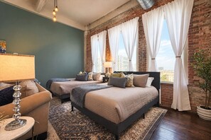 A hotel room with two beds, a sitting area with a lamp, and a view of the city. - The Bentley Collection - The Sinclair (Dallas)