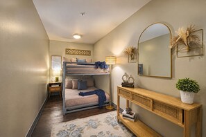 A compact bedroom with bunk beds, a bedside table with a lamp, a console table with decorative items, and a large mirror on the wall. - The Bentley Collection - The Sinclair (Dallas)
