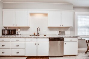 A kitchen with white cabinets, a granite countertop, a sink, a dishwasher, and a toaster. - Brick Road Bungalow 3/1 in South Overton! (Lubbock)