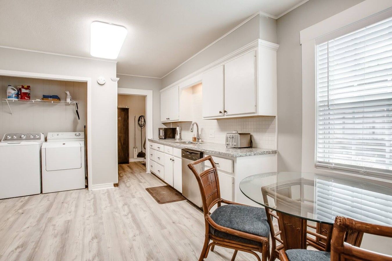 A modern kitchen with white cabinets, a built-in microwave, and a glass dining table with chairs.