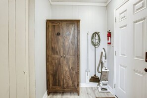 A hallway with a wooden door, a vacuum cleaner, a broom, and a fire extinguisher. - Brick Road Bungalow 3/1 in South Overton! (Lubbock)