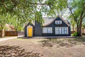 A two-story house with a dark exterior, a yellow front door, and a small attached garage. - Brick Road Bungalow 3/1 in South Overton! (Lubbock)