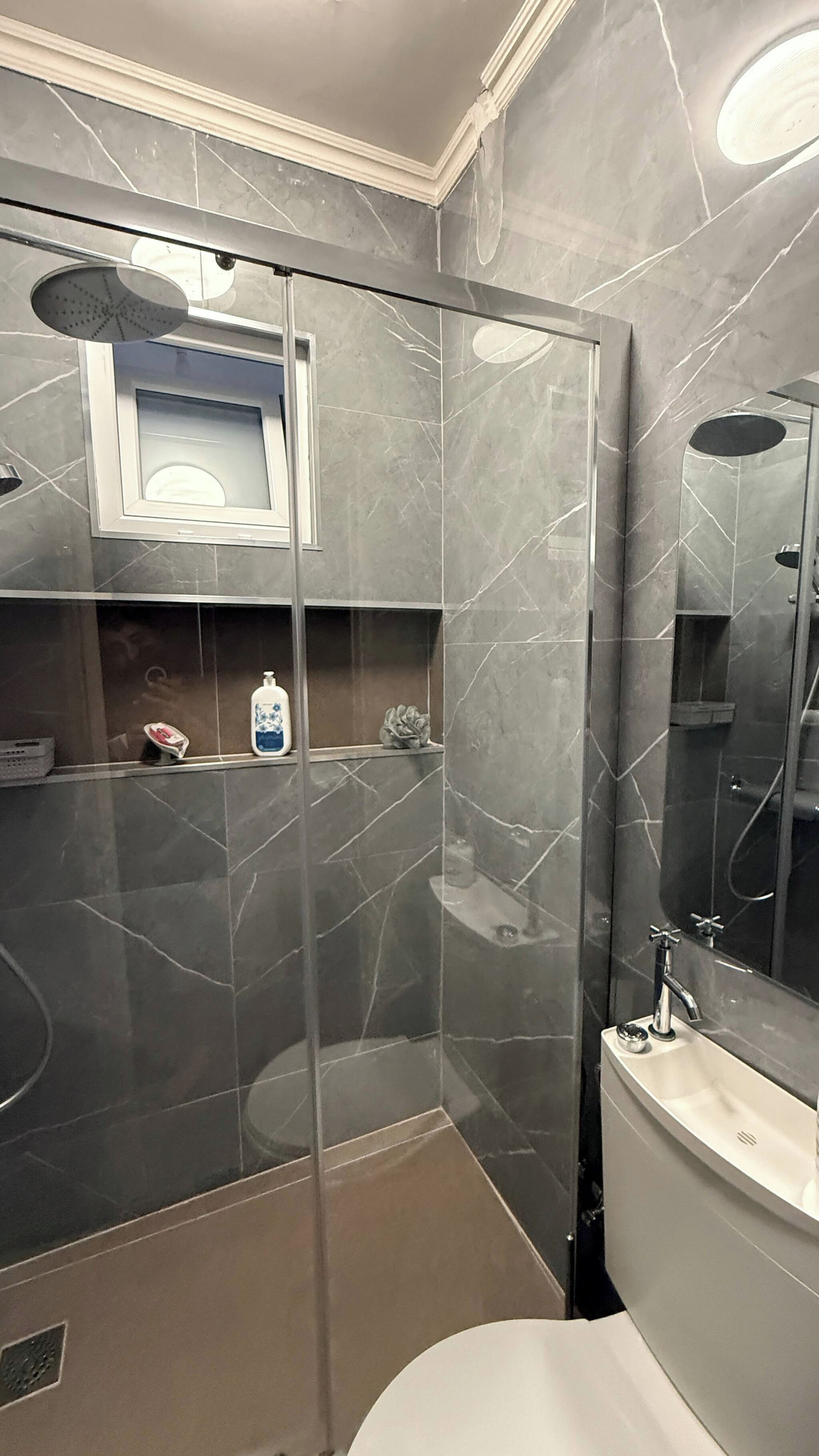 Un baño moderno con ducha de vidrio, lavamanos empotrado y espejo sobre el mueble de tocador.