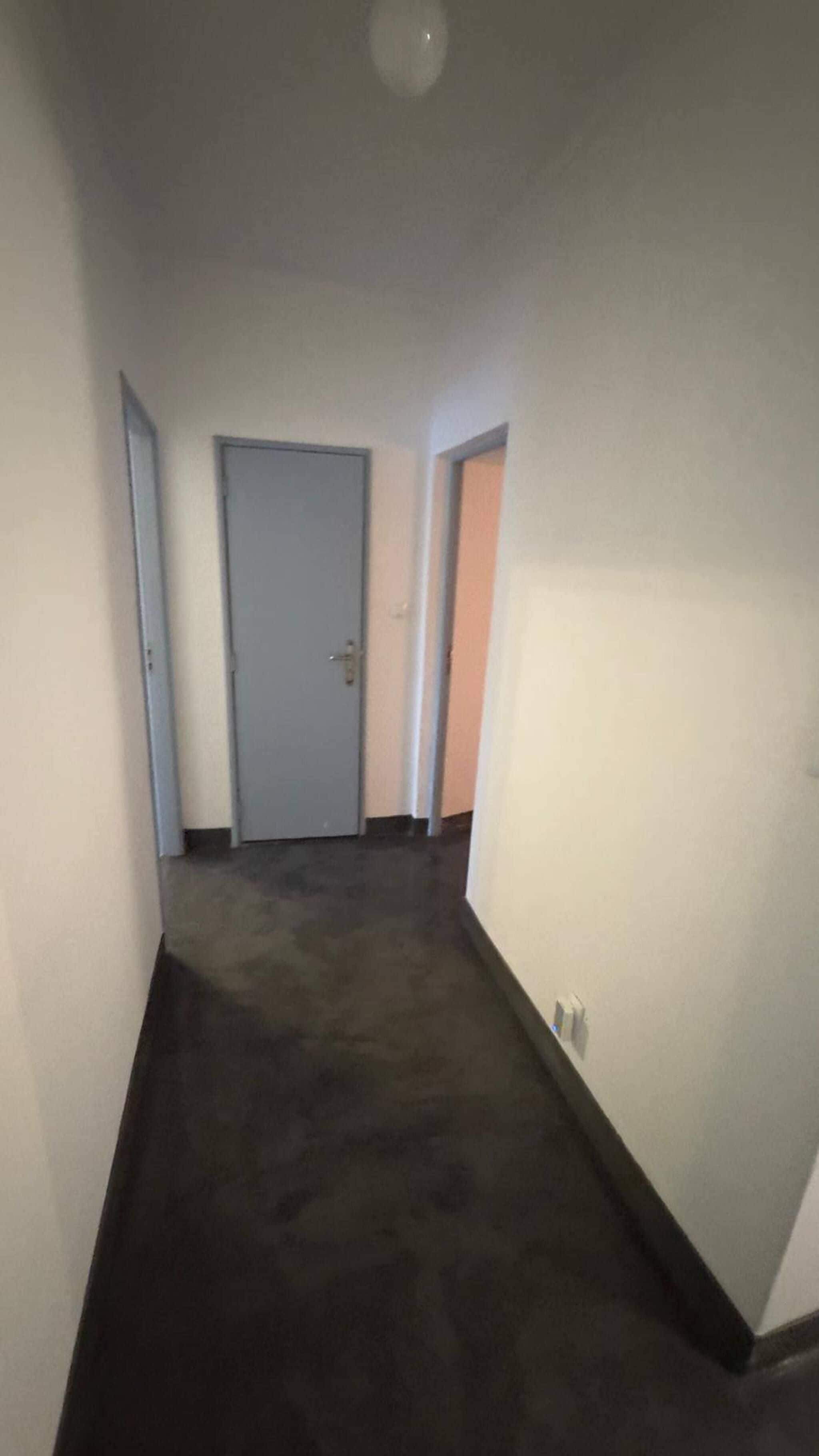 A hallway with a carpeted floor, a closed door, and a wall-mounted light fixture.
