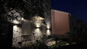 Un edificio de piedra con un persiano cerrado, iluminado por luces empotradas en la pared, y un cartel vacío.