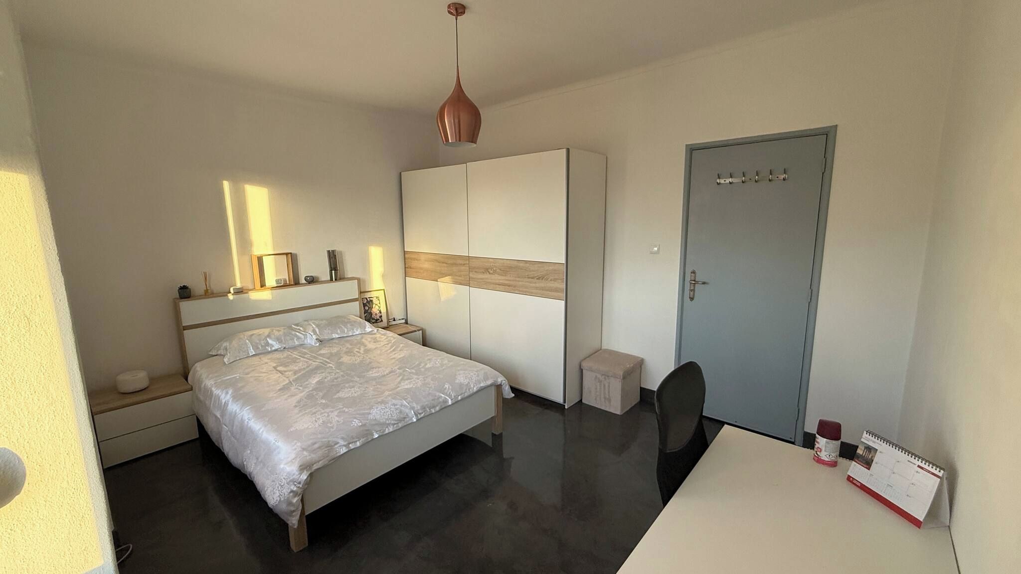 A modern bedroom with a bed, bedside tables, a wardrobe, a desk, and a door.