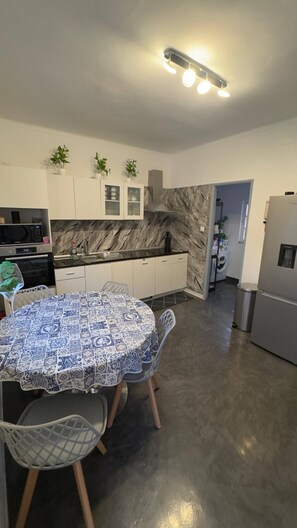 A modern kitchen with a dining area, featuring a marble backsplash, white cabinetry, and a round table with chairs.