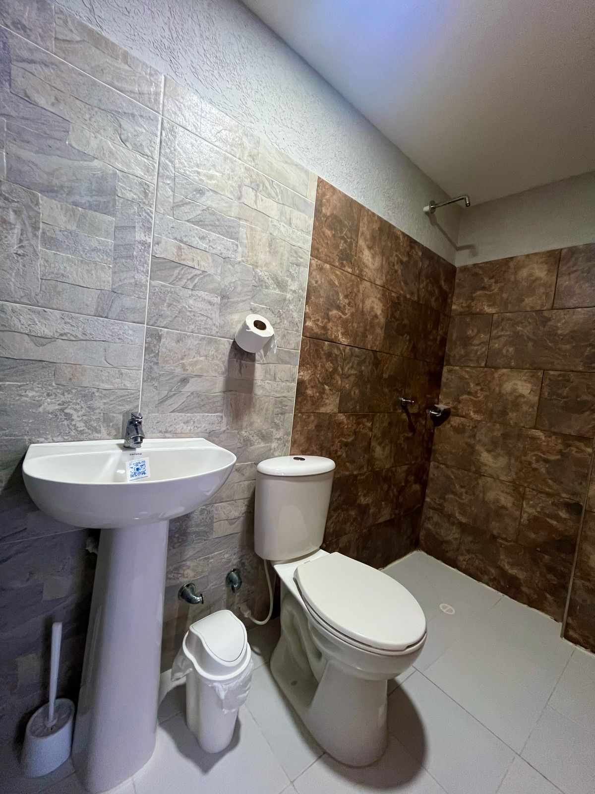 Et badeværelse med et pedalvask, toilet og bruseområde.