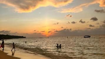 A beach scene with a sunset, people walking along the shore, and a boat in the distance.