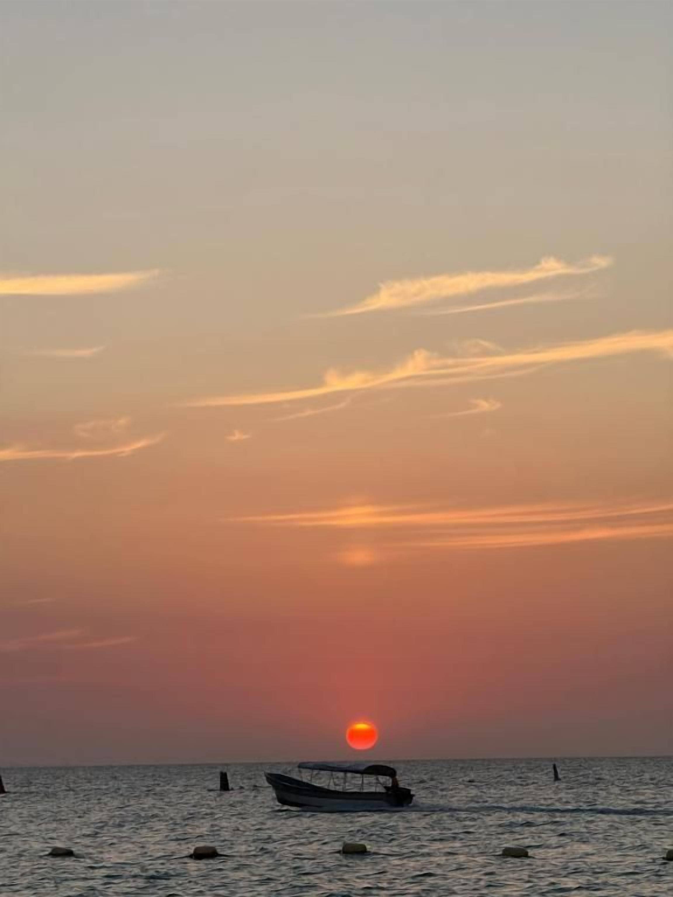 Un atardecer sobre el océano con un barco y boyas.