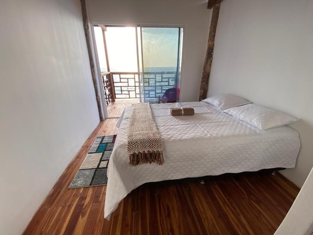 Un dormitorio con cama, vista al mar desde un balcón y suelo de madera.