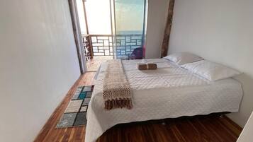 Un dormitorio con cama, vista al mar desde un balcón y suelo de madera.